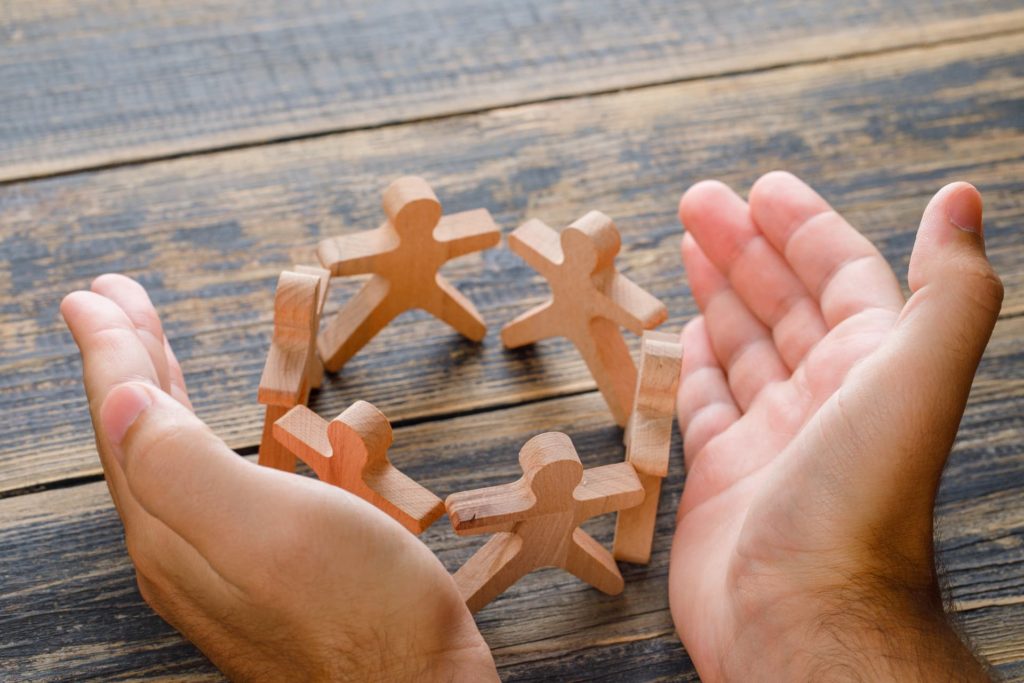 business success concept on wooden table top view hands protecting wooden figures of people