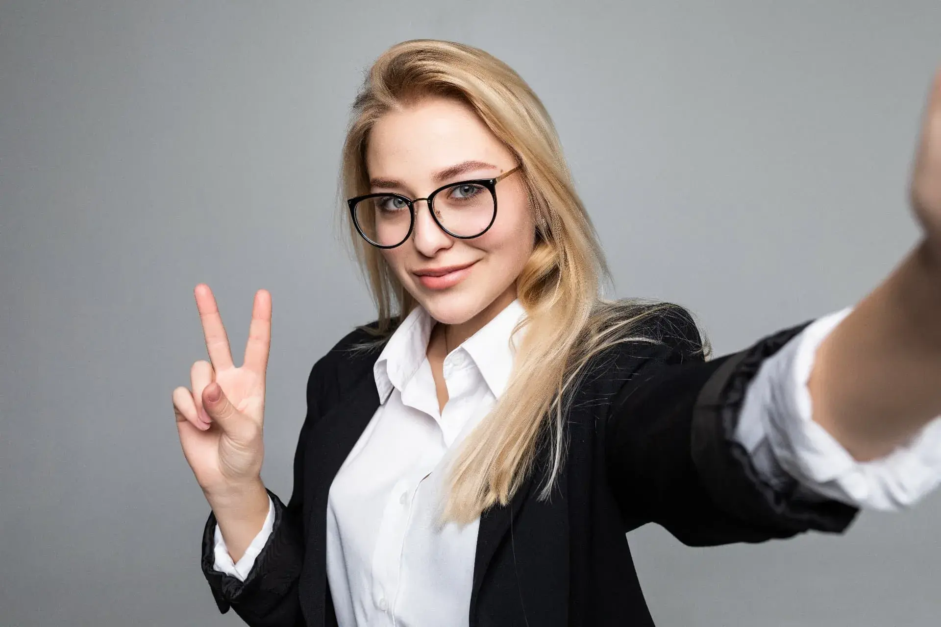 portrait business woman making selfie using smart phone internet gesturing peace symbol having video call online grey wall 1